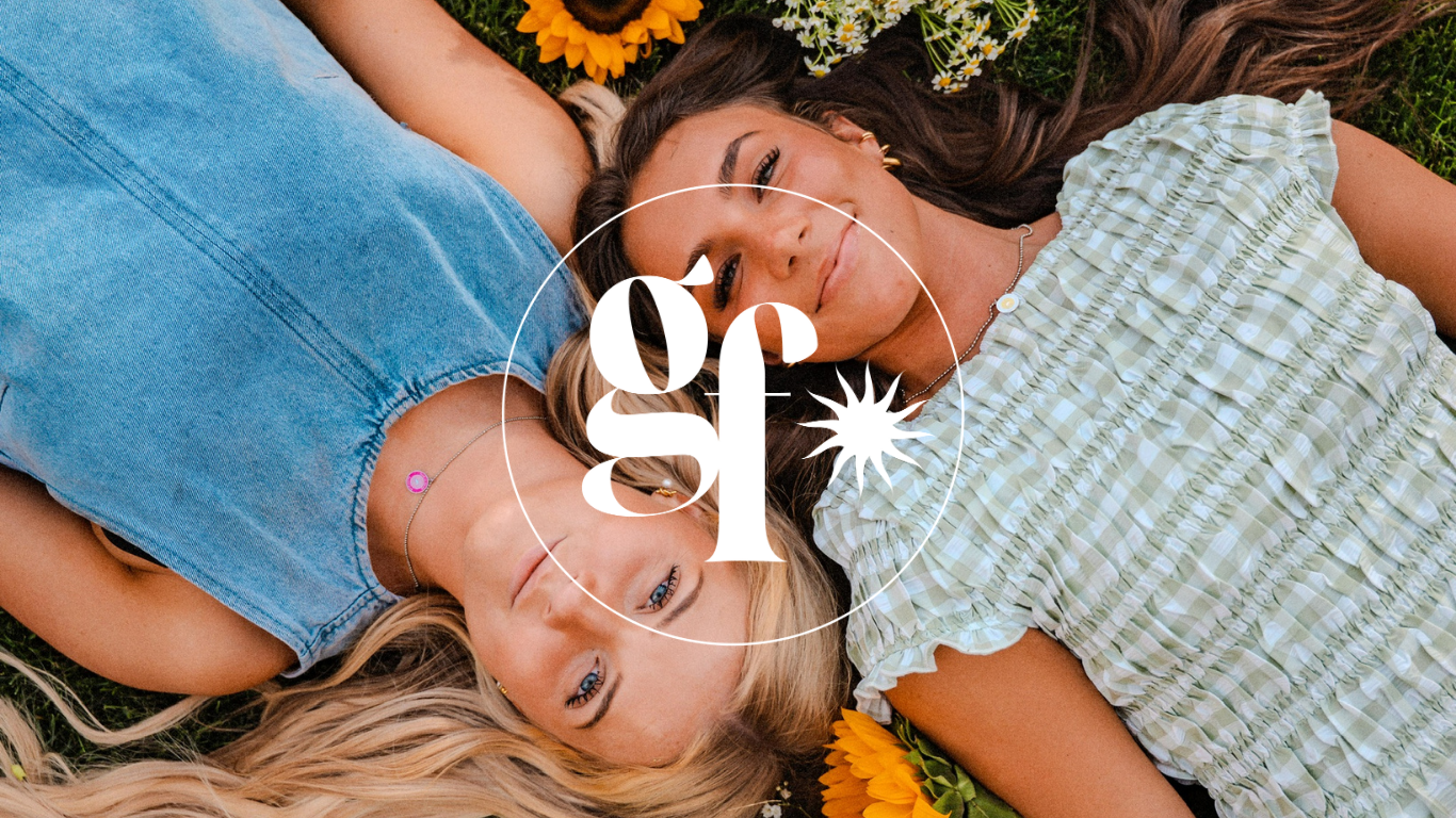 Two people lying on grass with flowers, wearing denim and a checkered dress, surrounded by a circular logo.