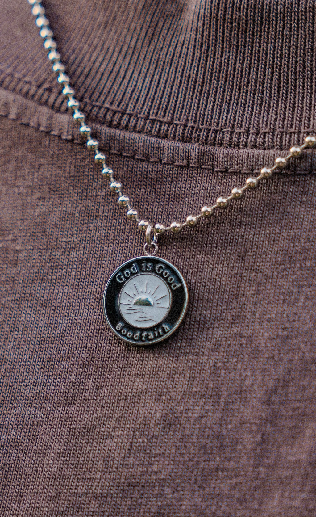 silver necklace with black and silver pendant hanging on brown shirt