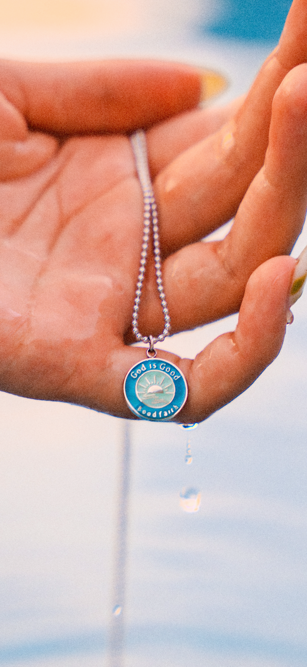 Necklace with a blue pendant held in a hand against a blurred pool background
