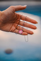 Hand holding a necklace with a pink pendant with a blurred background