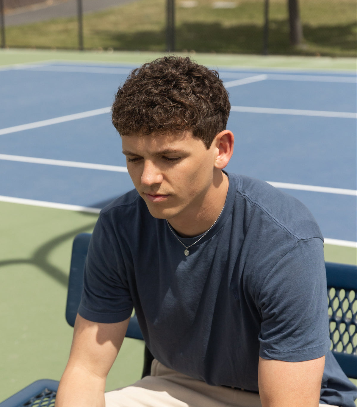 a young man wearing a silver god is good necklace on a pickle ball court.