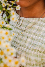 Person wearing a green checkered dress with a necklace, surrounded by daisies.